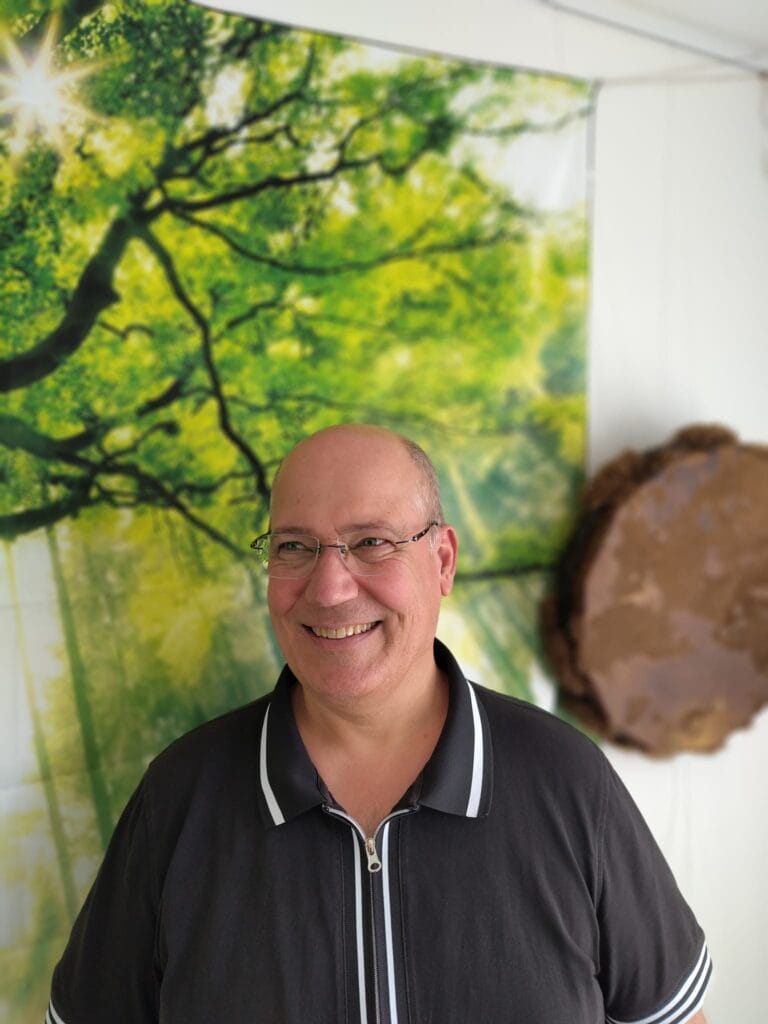 Frank Ouwerkerk in zijn praktijkruimte, met een bosfoto aan de wand