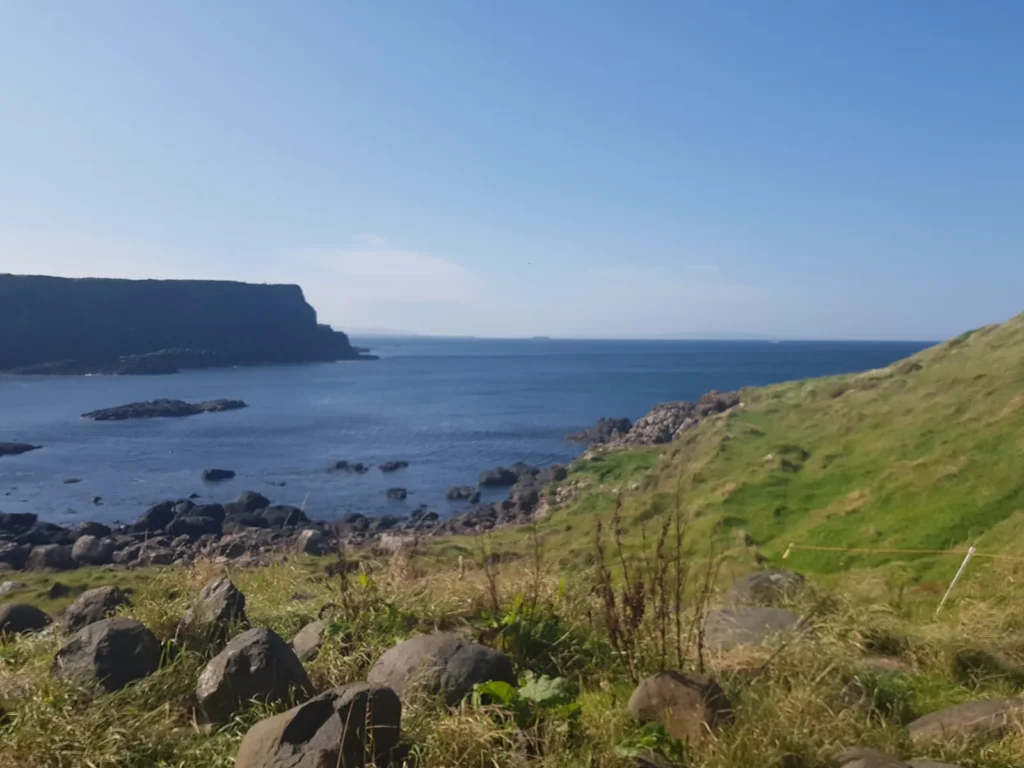 Uitzicht over de rotsachtige kust van Noord-Ierland, met groene heuvels, donkere rotsen en een blauwe zee
